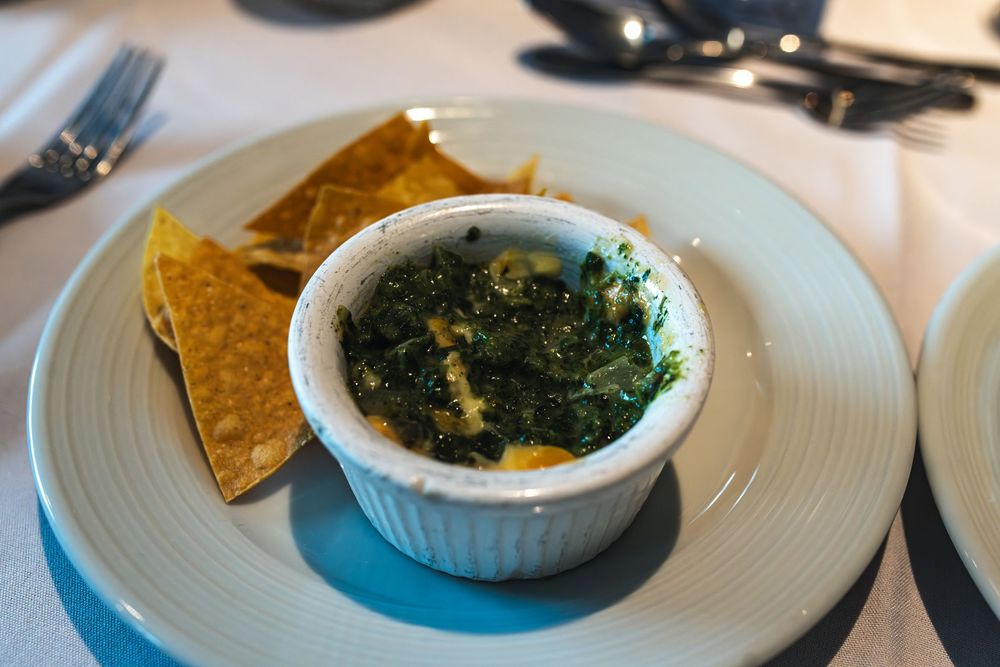 Spinach dip in a white ramekin served with crispy tortilla chips on a light blue ceramic plate.