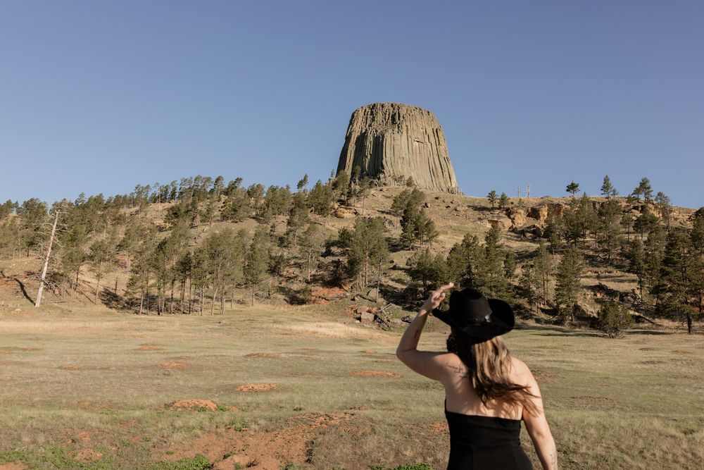 Woman in black hat gazing at Devils Tower National Monument in Wyoming on a sunny day.