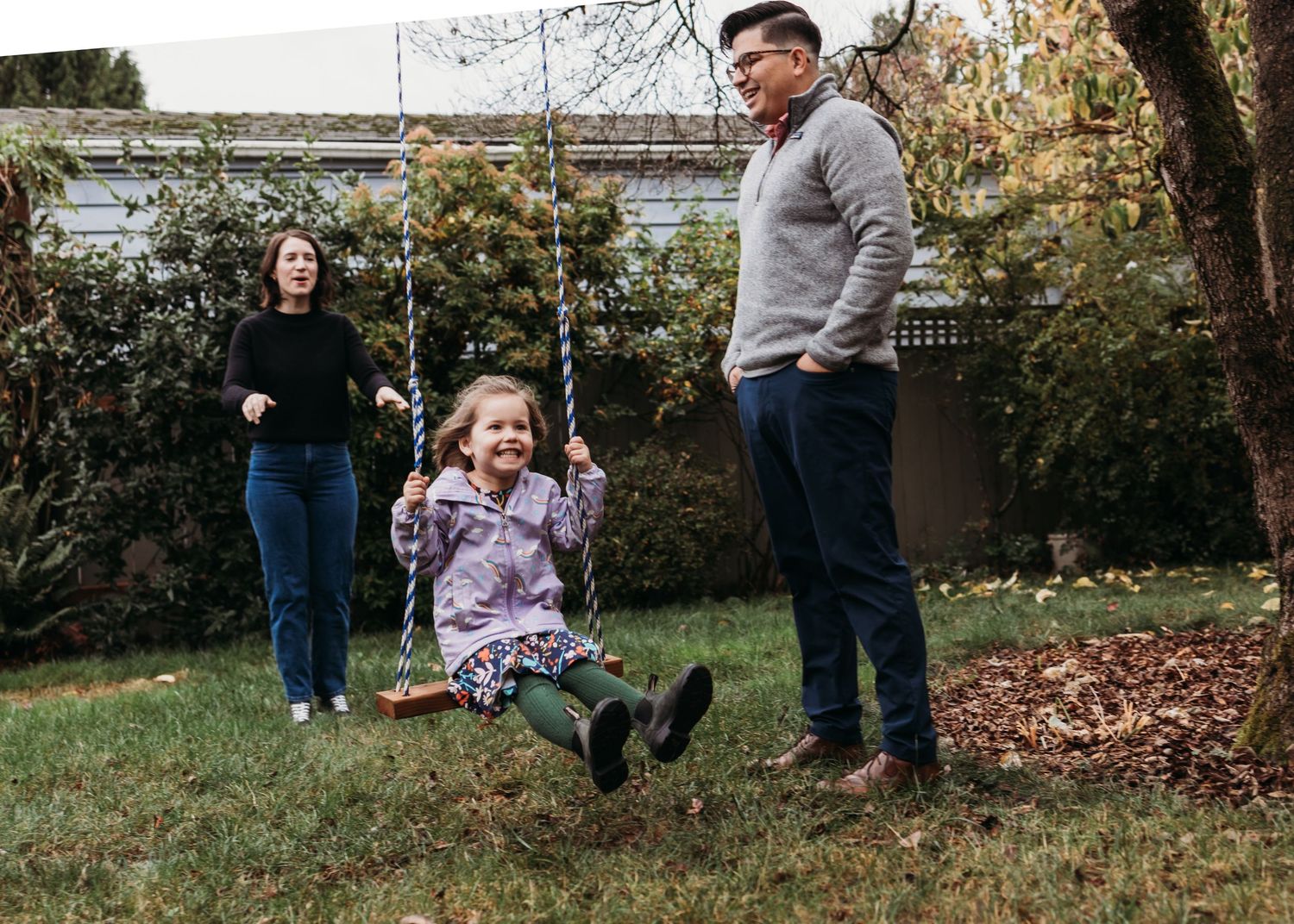 Family enjoying outdoor playtime with young girl on wooden swing in autumn backyard garden.