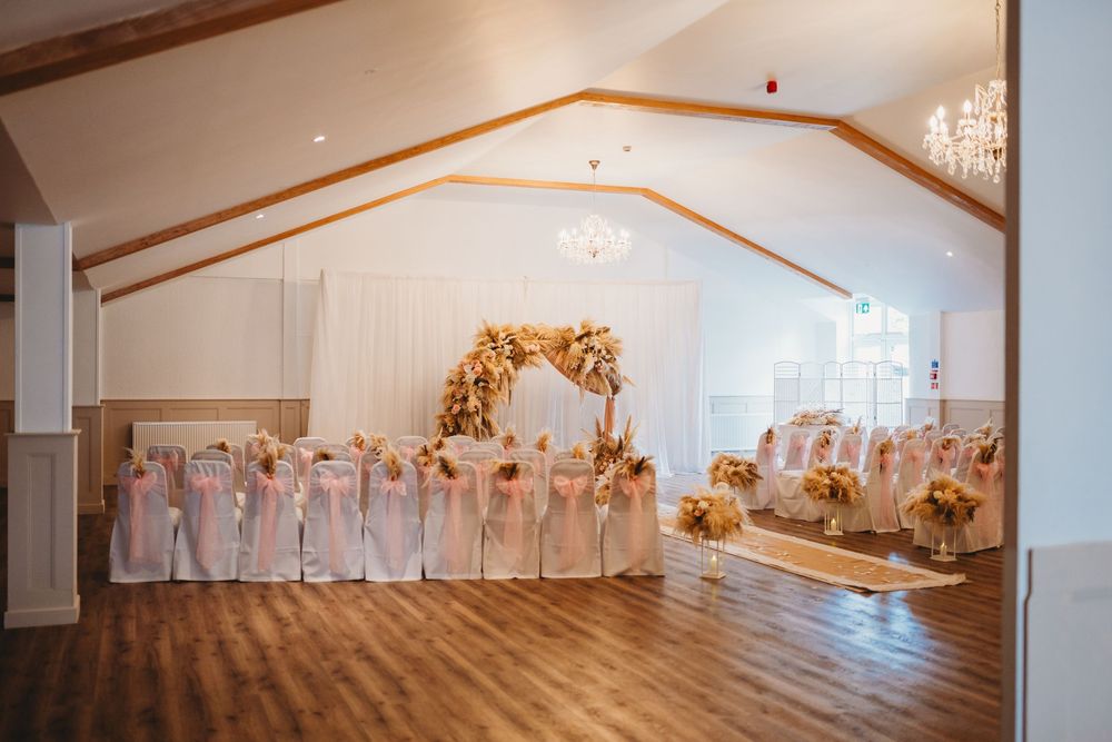 Elegant wedding venue with floral arch, white chair covers, and chandelier lighting on hardwood floors.