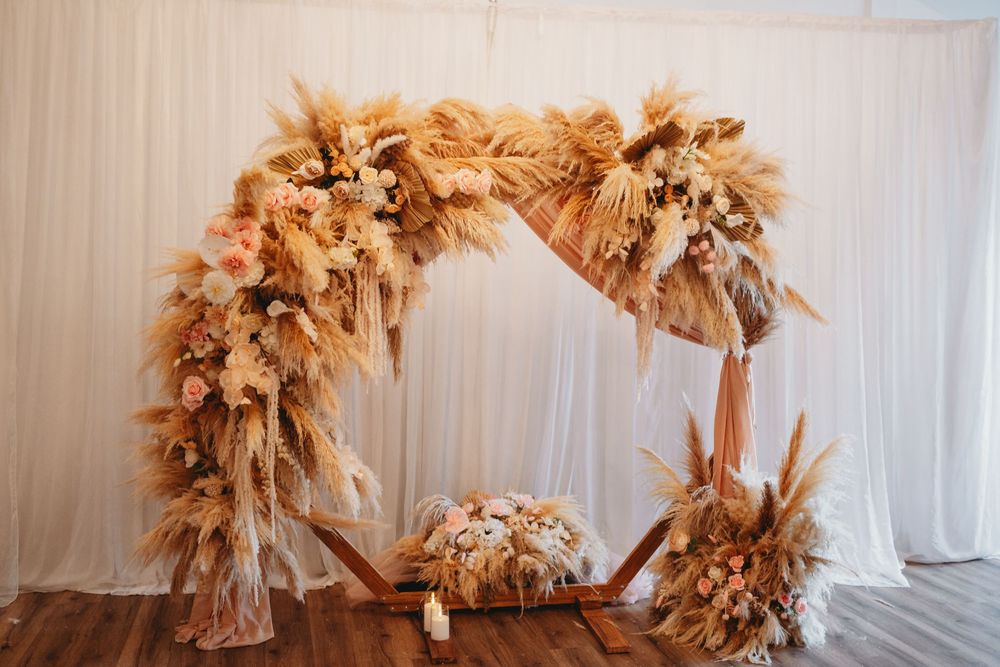 Boho wedding arch adorned with pampas grass, dried flowers, and peach blooms on a wooden hexagonal frame.