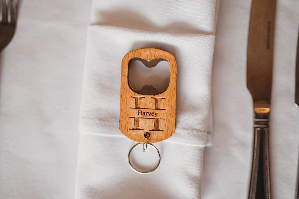 Personalized wooden bottle opener keychain engraved with the name Harvey, placed on a white napkin at a wedding table setting.