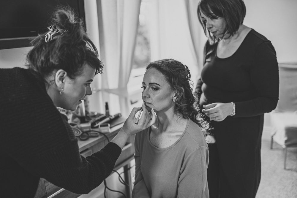 Bride getting hair and makeup done by two stylists in black and white wedding preparation photo.