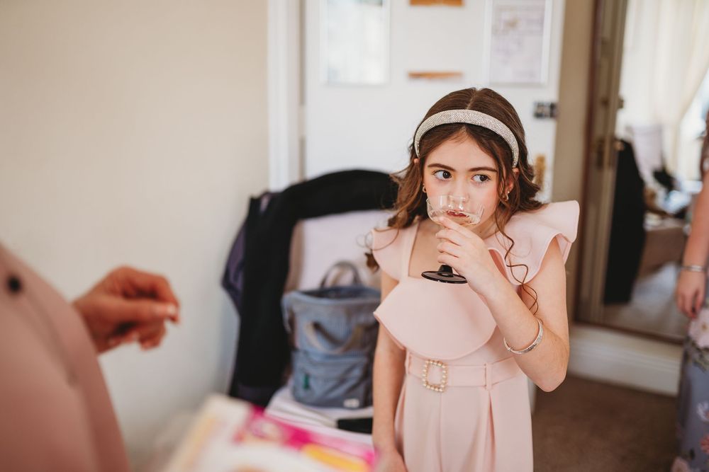 Young flower girl in pink dress holding purse during wedding preparations.