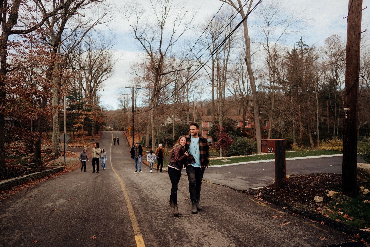 Couple walking hand-in-hand on a tree-lined road in autumn, with other visitors strolling in the background.