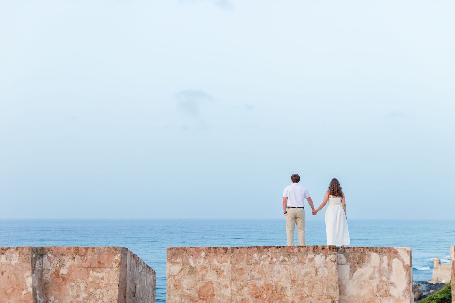 Couple standing on the fort walls with the ocean in the background. Engagement photo session in Old San Juan, Puerto Rico.