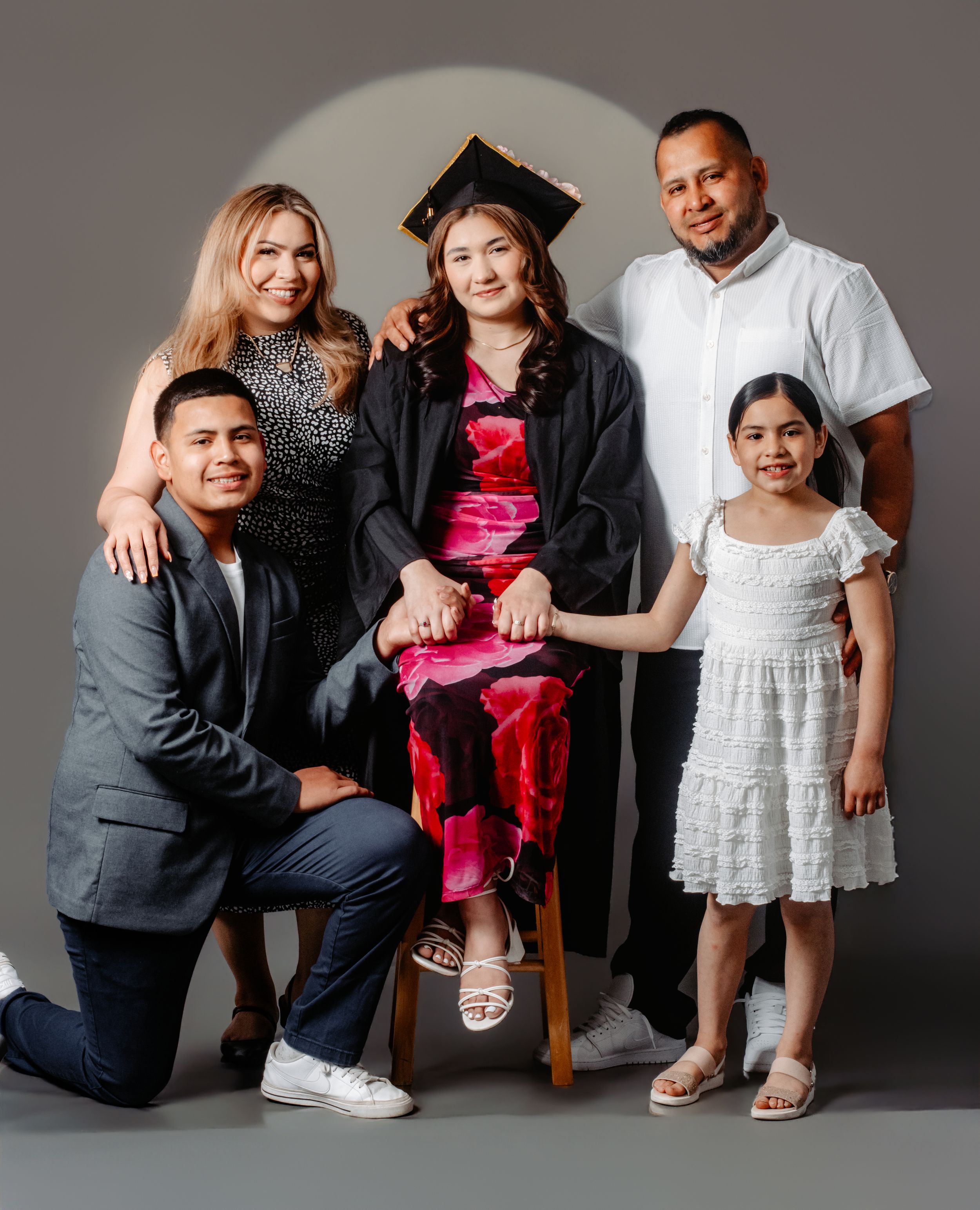 Family of five posing for a graduation portrait, with graduate in cap and gown seated at center.