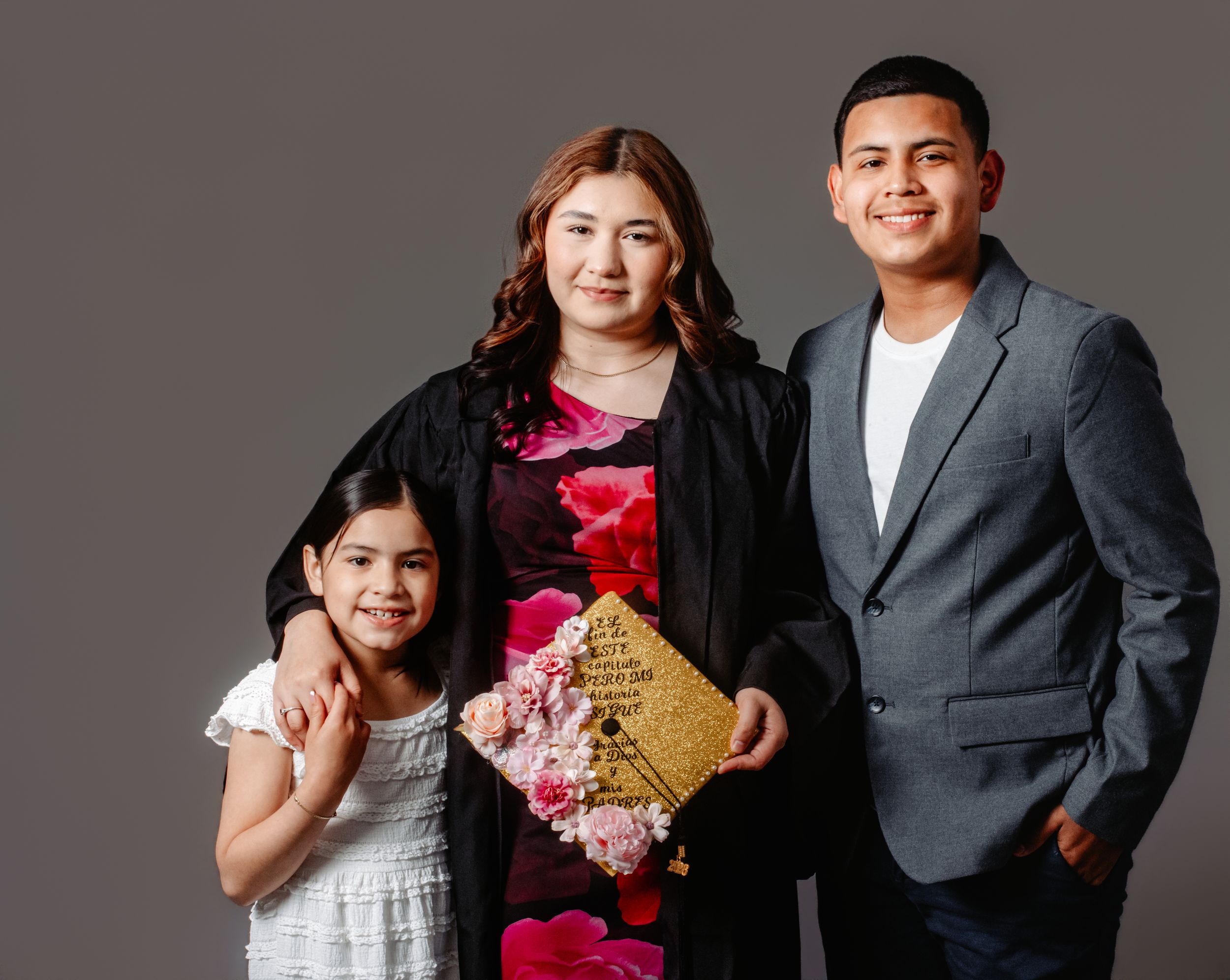 A woman in graduation gown poses with two children holding a gold diploma in a studio portrait.