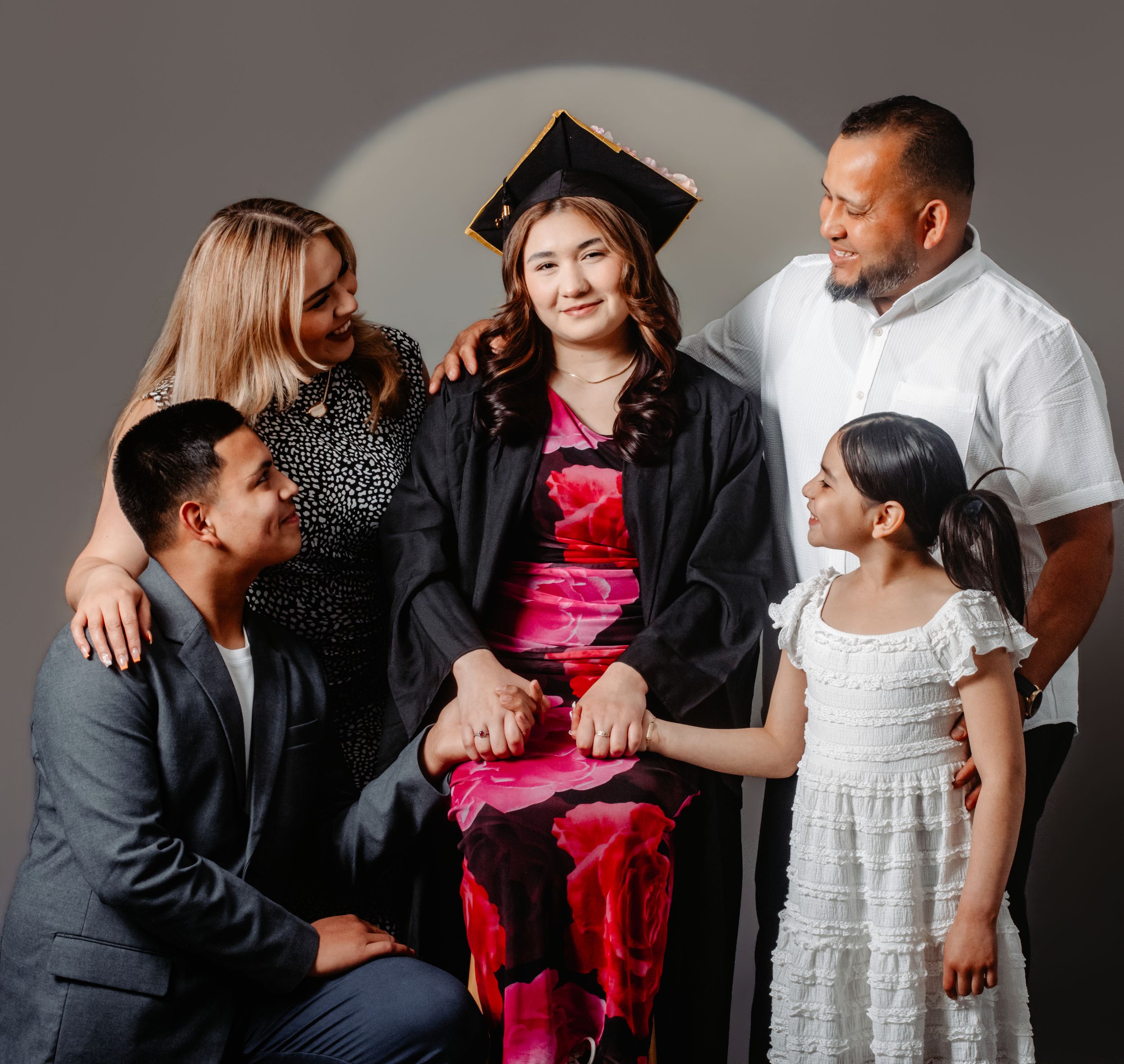 A graduate in cap and gown poses with her proud family of five in a professional studio portrait.