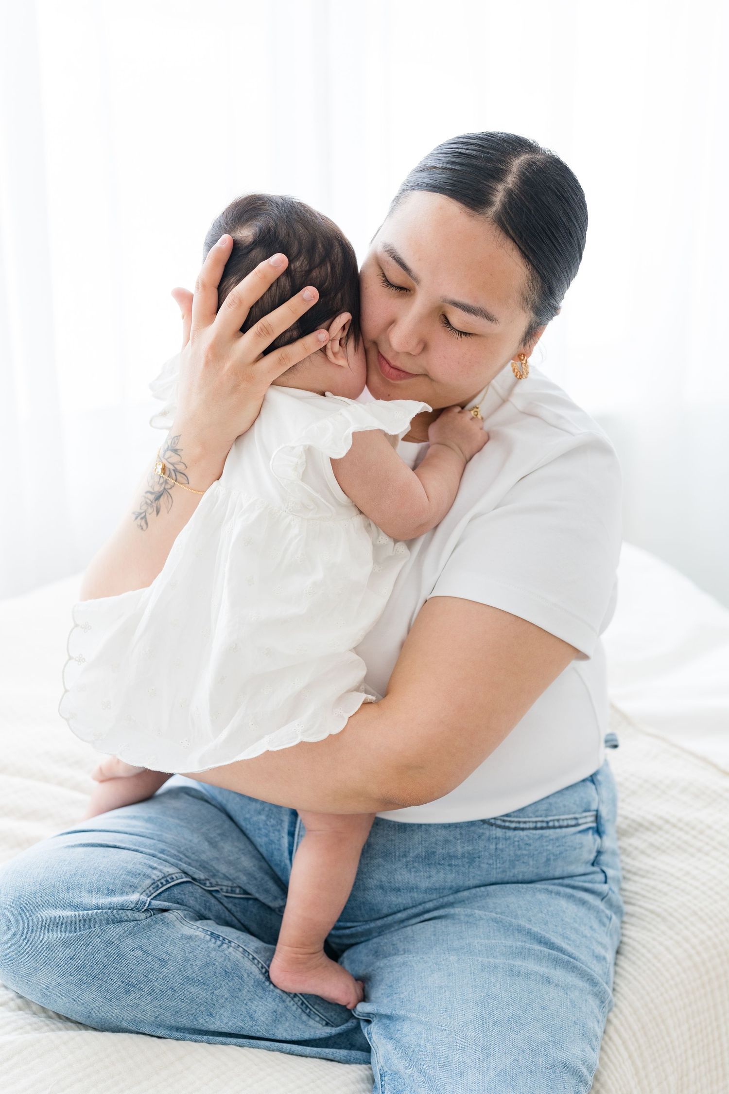 Maman tenant avec amour sa petite fille dans ses bras, les yeux fermés, savourant le moment d’intimité dans la lumière du studio