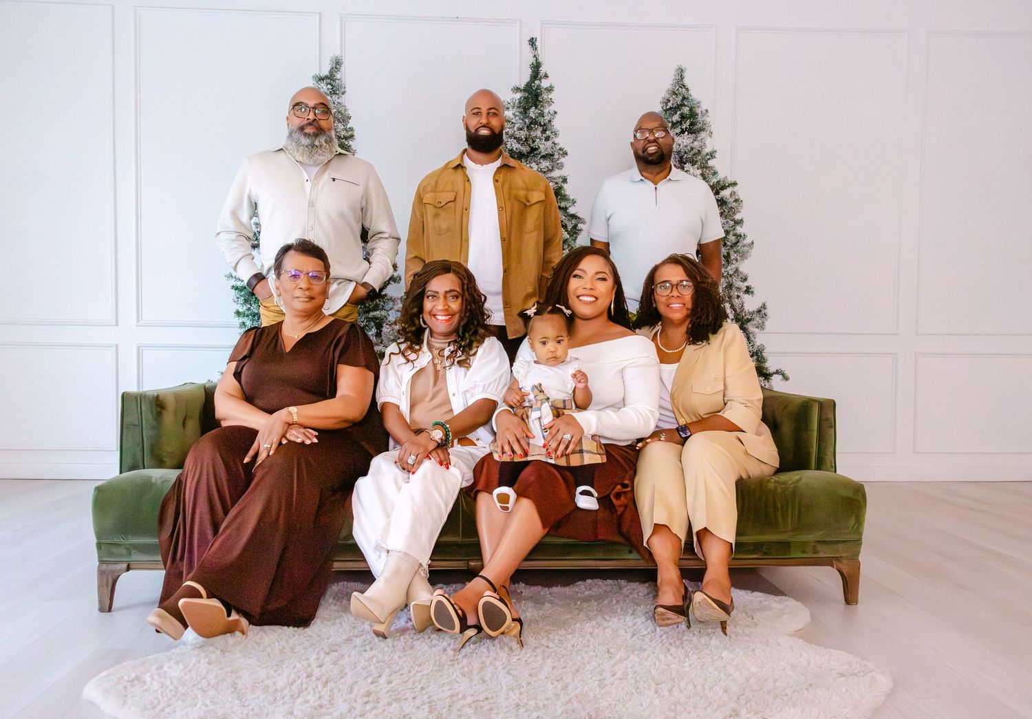 Family Christmas portrait with eight members posing in front of white trees on a green velvet sofa.