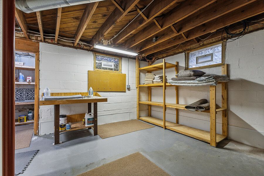 Unfinished basement workshop area with wooden shelving units and workbench on concrete floor.