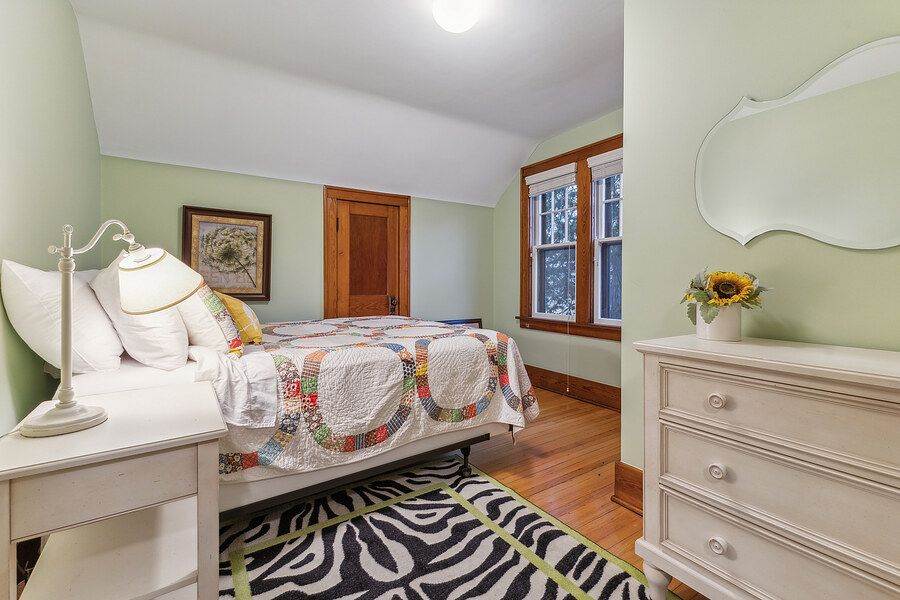 Cozy bedroom with green walls, white dresser, zebra print rug, and colorful quilt on bed with hardwood floors.