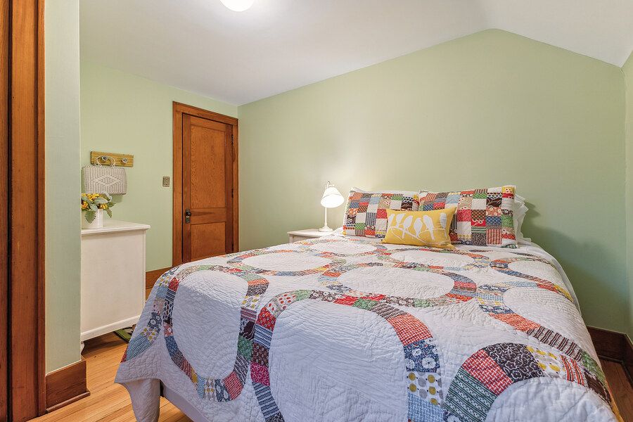 Cozy bedroom with a colorful patchwork quilt, light green walls, and hardwood floors.