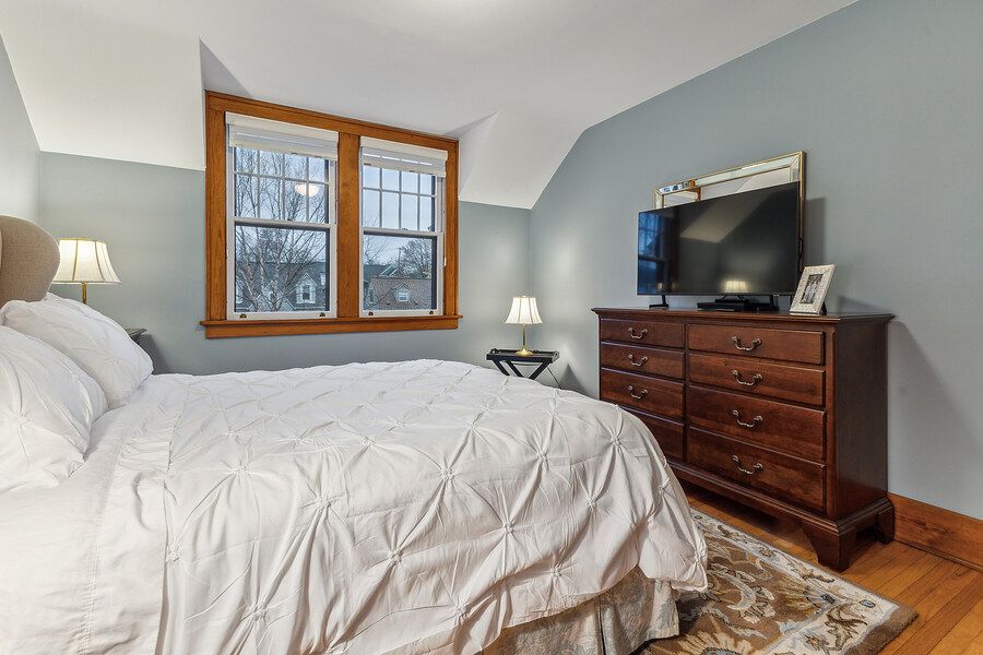 Cozy bedroom with vaulted ceilings, white bedding, hardwood floors, and a dark wood dresser with TV.