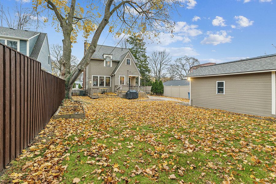 Backyard covered in autumn leaves with a wooden fence, patio, and detached garage under a blue sky.