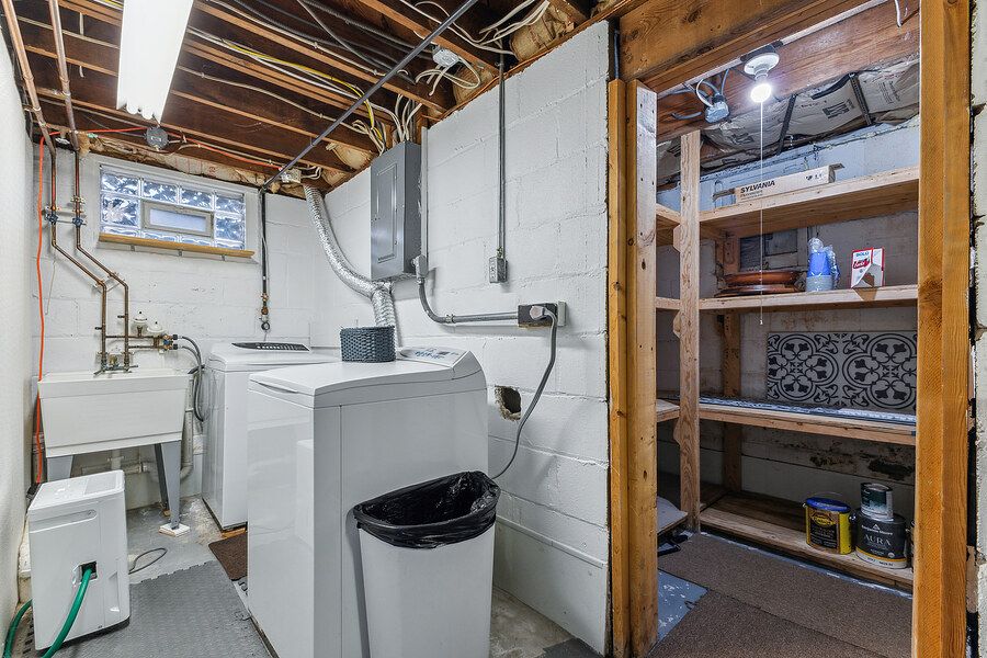 Unfinished basement laundry room with washer, dryer, utility sink, open shelving, and exposed ceiling joists.