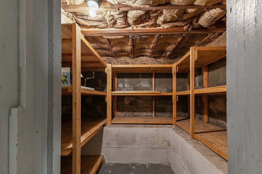 Basement storage room with wooden shelving units and exposed ceiling insulation.