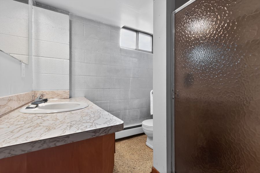 Bathroom with marble countertop vanity, cinder block walls, frosted glass shower door, and a toilet.
