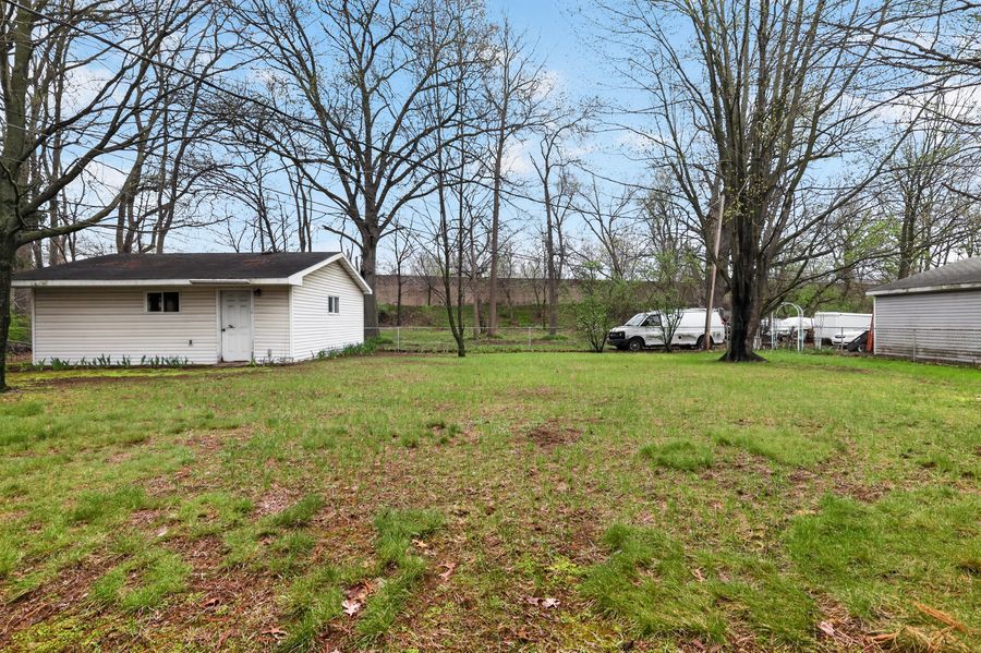 Spacious backyard with lush green grass, mature bare trees, and a white outbuilding.