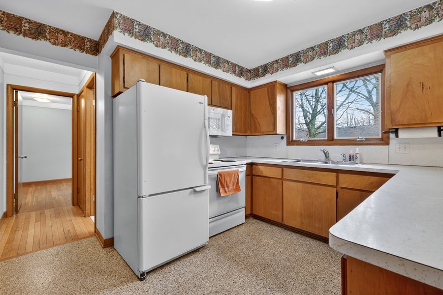 Bright kitchen with oak cabinets, white appliances, tile countertops, and a window above the sink.