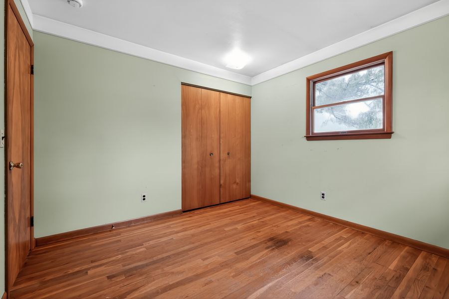 Spare bedroom with hardwood floors, crown molding, wooden closet doors, and a single window with natural light.