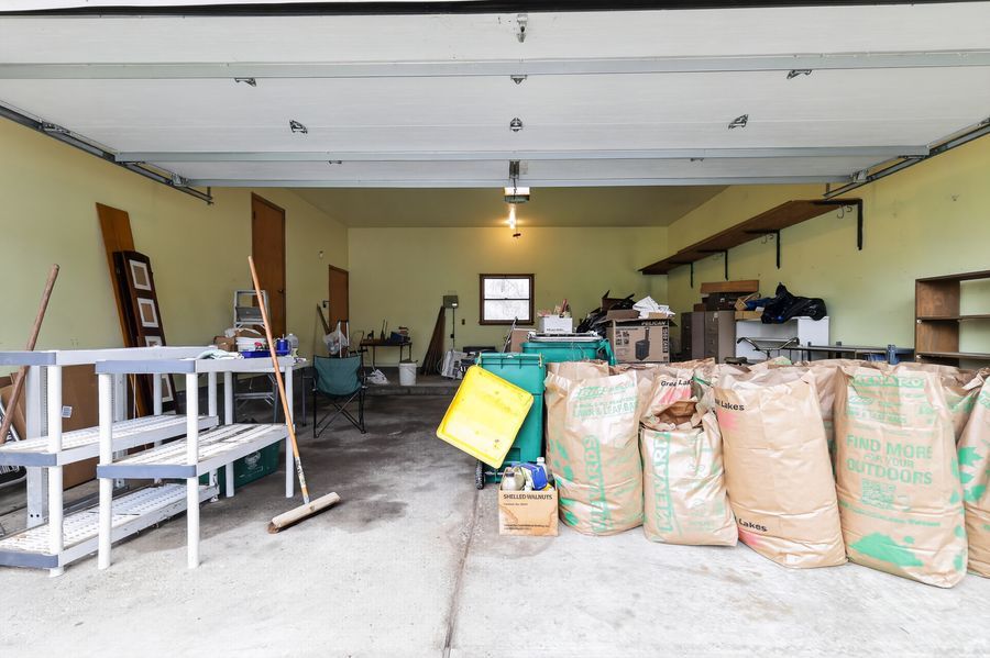 Open garage filled with bulk material bags, shelving units, and various stored items on a concrete floor.