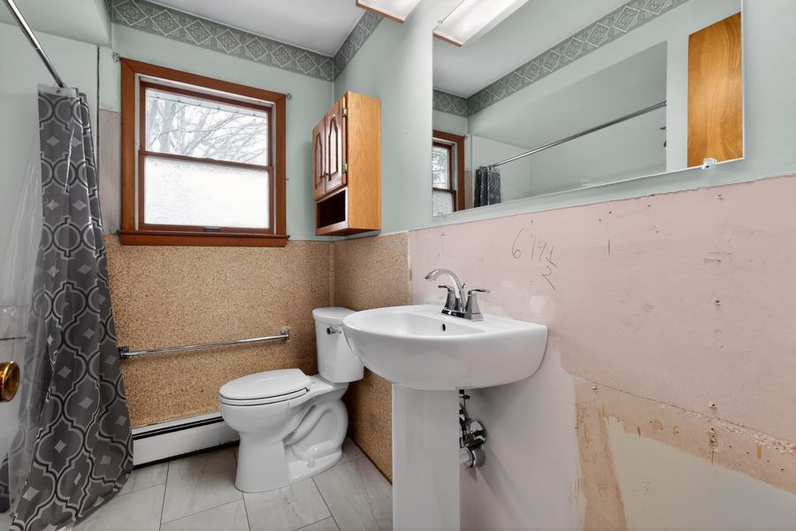 Vintage bathroom with pedestal sink, toilet, shower with curtain, wall-mounted cabinet, and pink tile wainscoting.