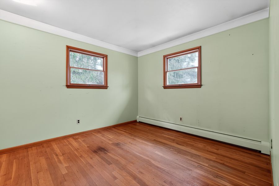 Empty room with light green walls, hardwood floors, two windows with wood trim, and a baseboard heater.