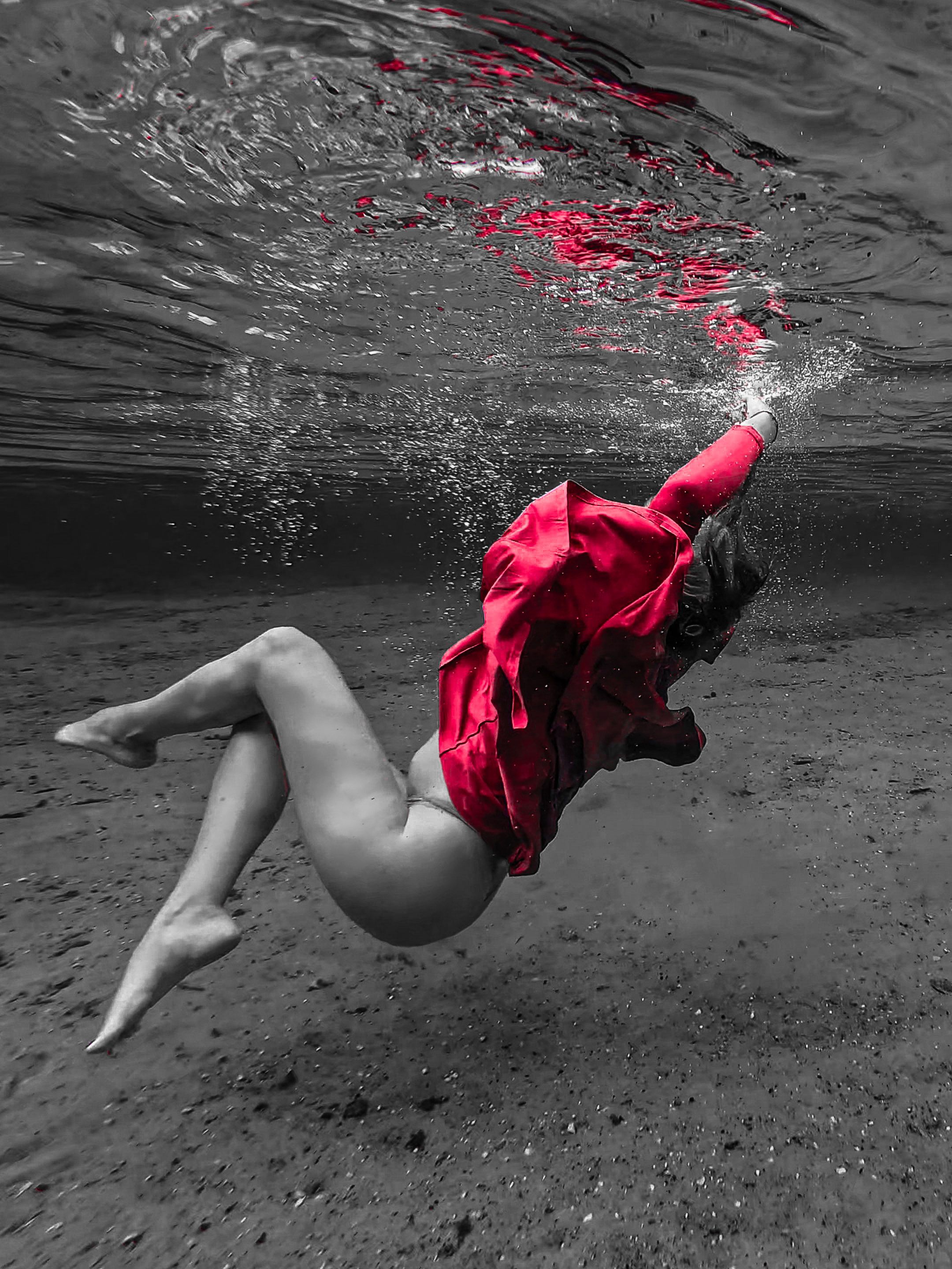 Woman in red dress floating underwater in black and white photography, creating a dramatic contrast.