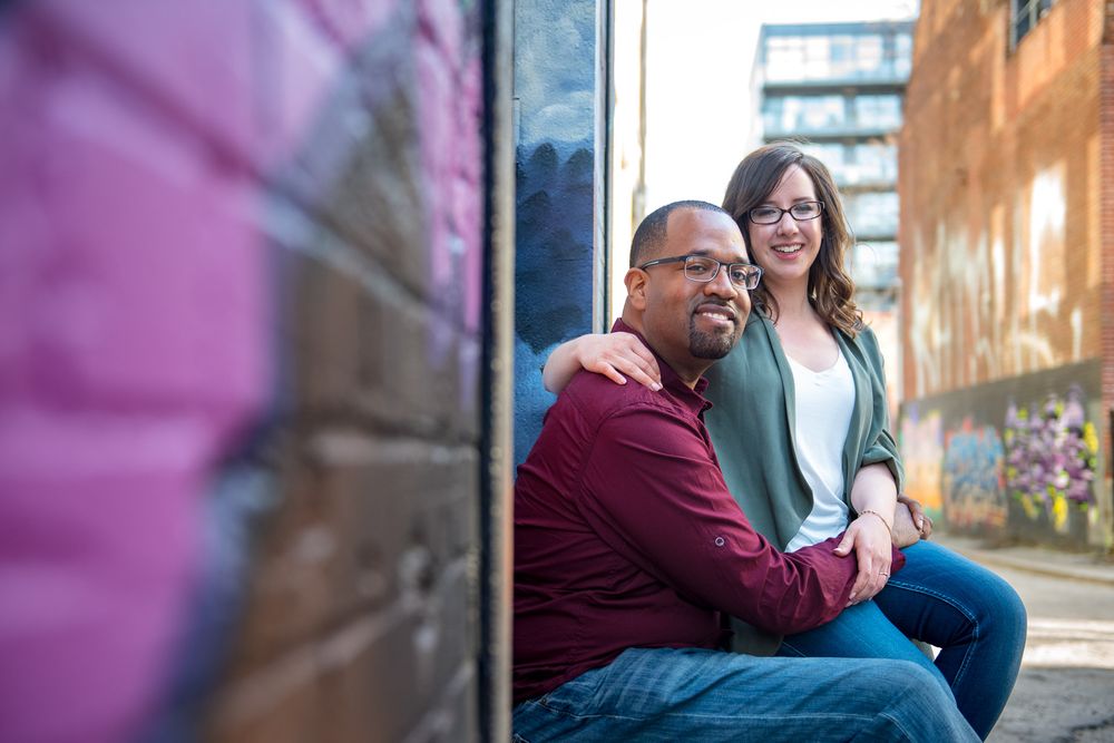 Smiling couple sitting together in an urban alley, woman with arm around mans shoulder in Graffity Alley in Toronto..