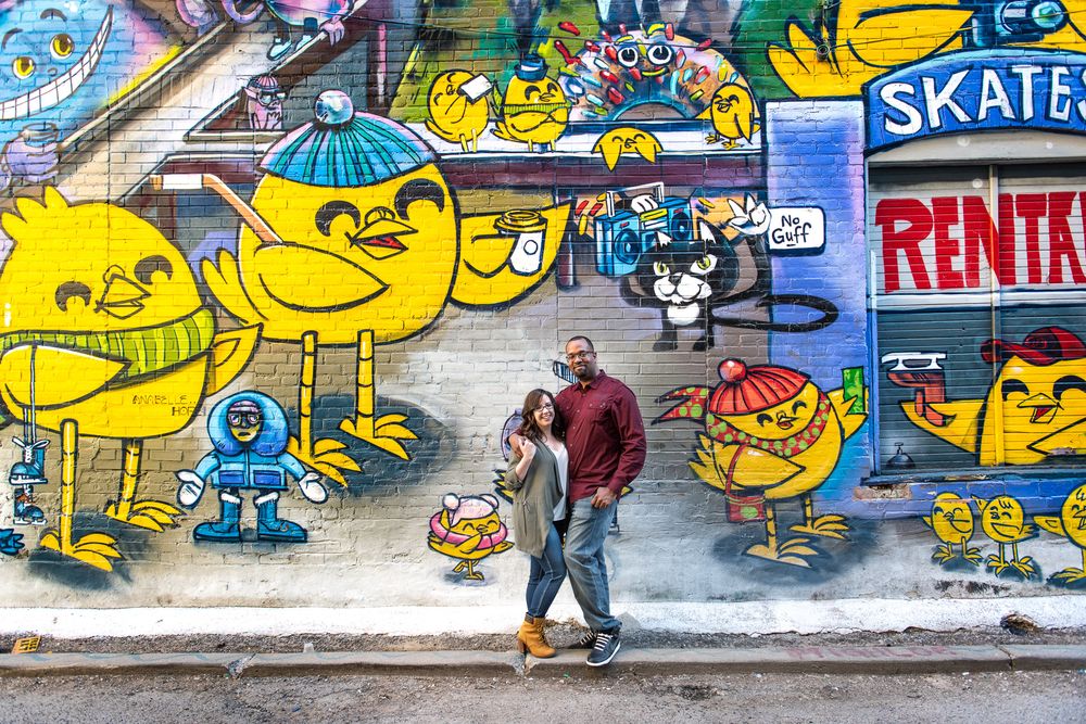 Couple posing together in front of colorful cartoon graffiti mural near skate rental shop in Graffity Alley in Toronto..