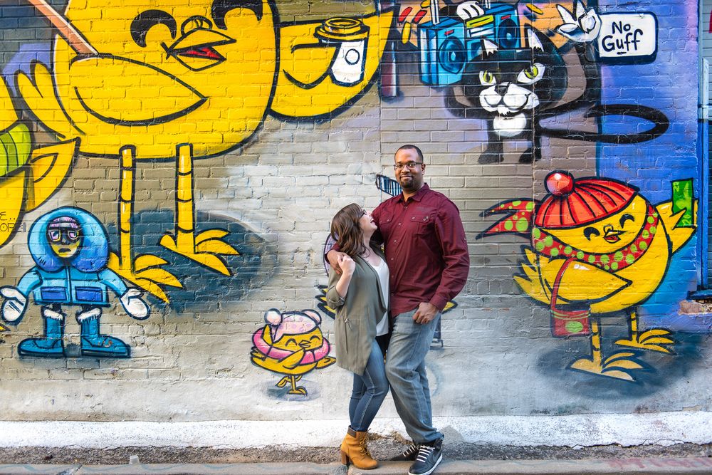 Couple embracing in front of vivid street art mural with cartoon characters in urban alley in Graffity Alley in Toronto..