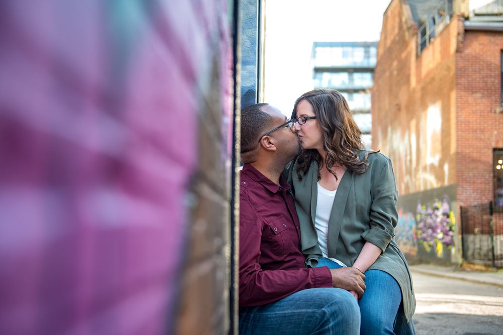 Couple sharing a romantic kiss while seated in an urban alleyway surrounded by graffiti walls in Graffity Alley in Toronto..
