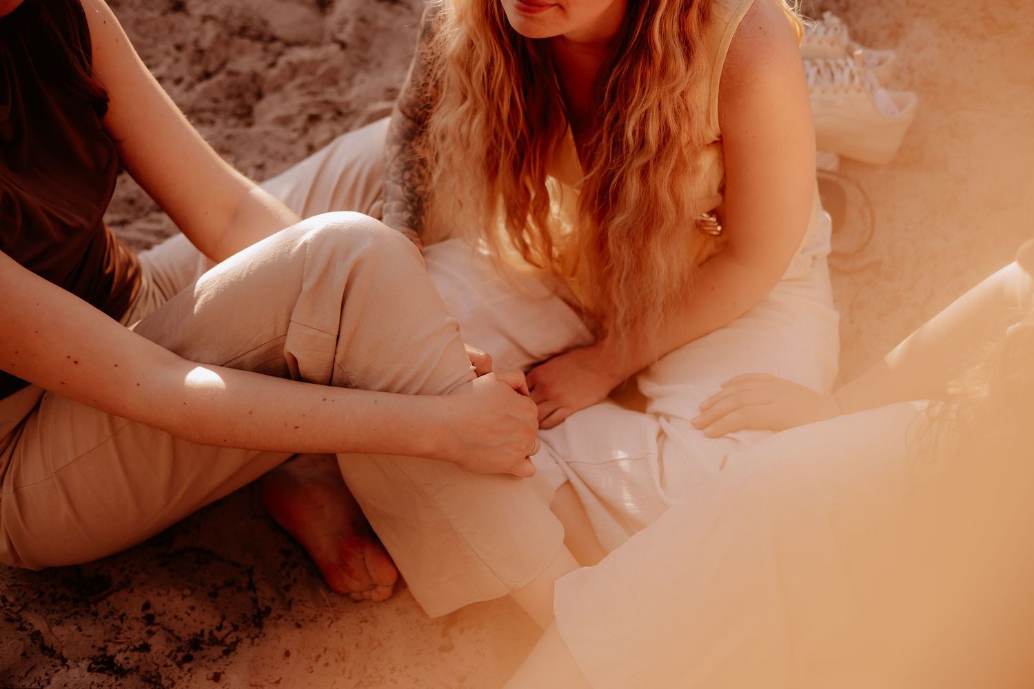 Close-up of people sitting barefoot on sandy ground in warm golden sunlight in a forest.
