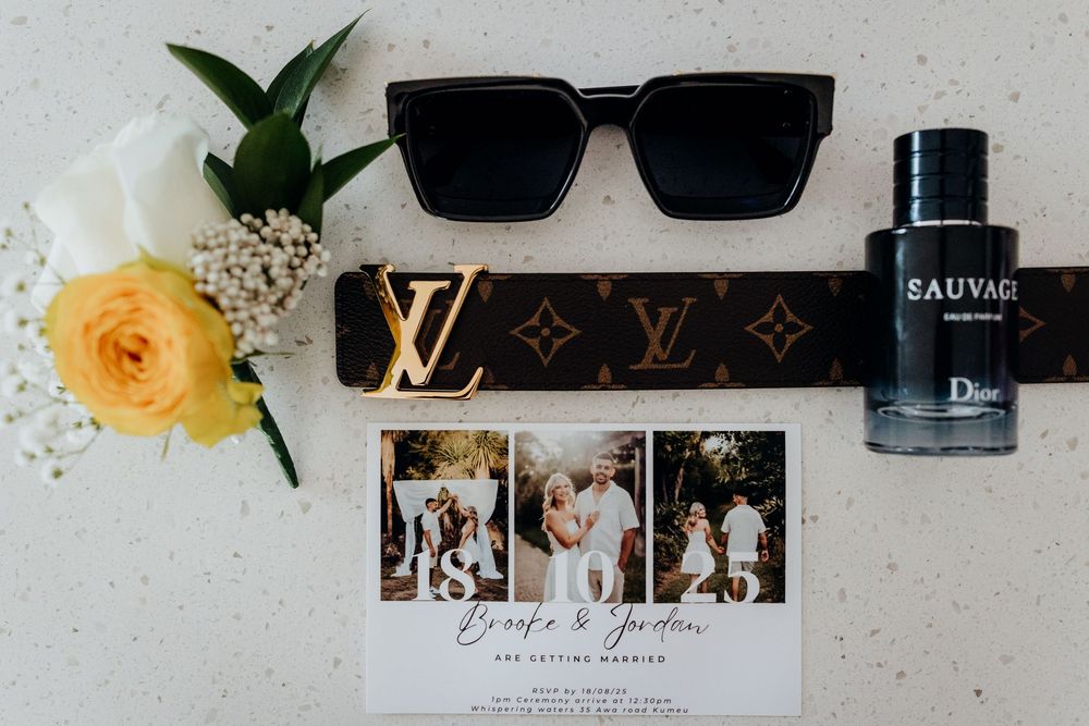 Louis Vuitton belt, black sunglasses, Dior Sauvage cologne, and wedding invitation flat lay with yellow roses.