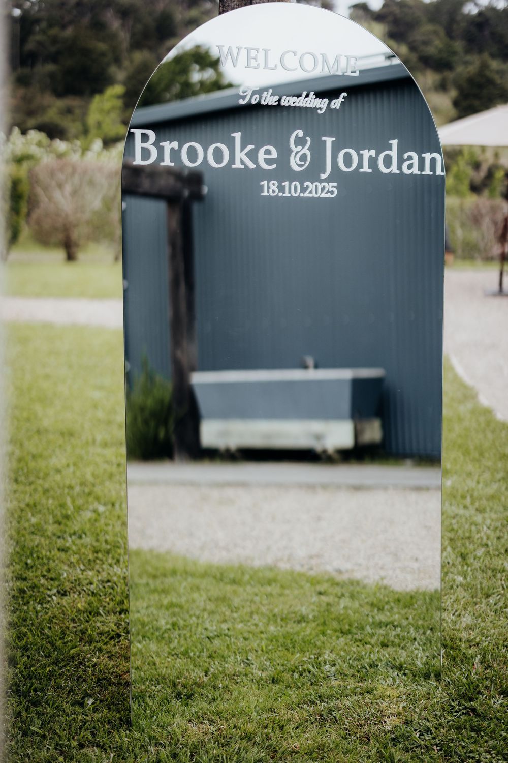 Elegant arched mirror wedding welcome sign for Brooke and Jordan on 18.10.2025 on a green lawn.