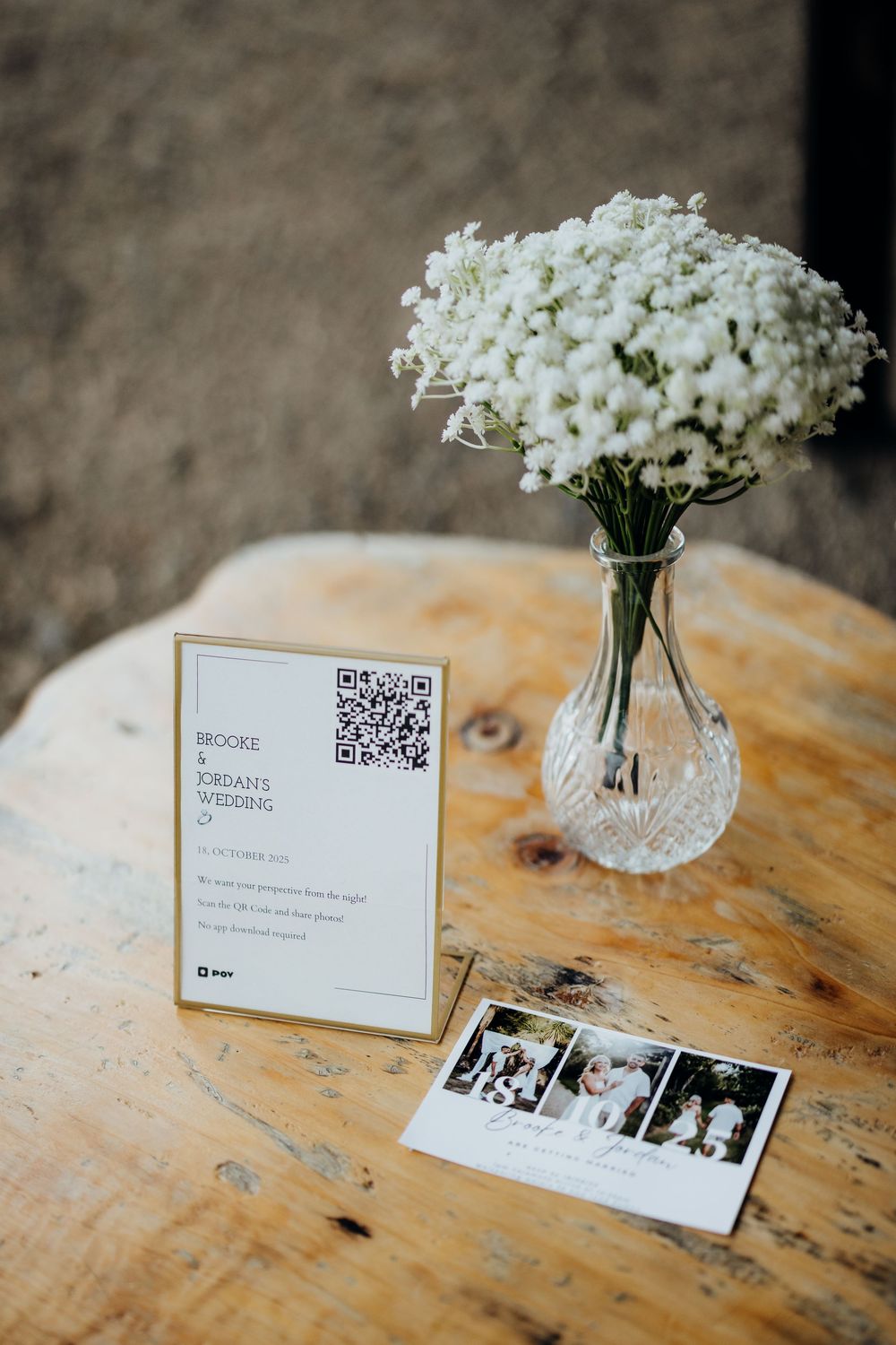 Brooke and Jordan wedding sign with QR code beside baby's breath flowers in crystal vase on rustic table.