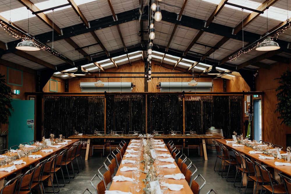 Elegant rustic wedding reception venue with long decorated tables and industrial ceiling in barn.
