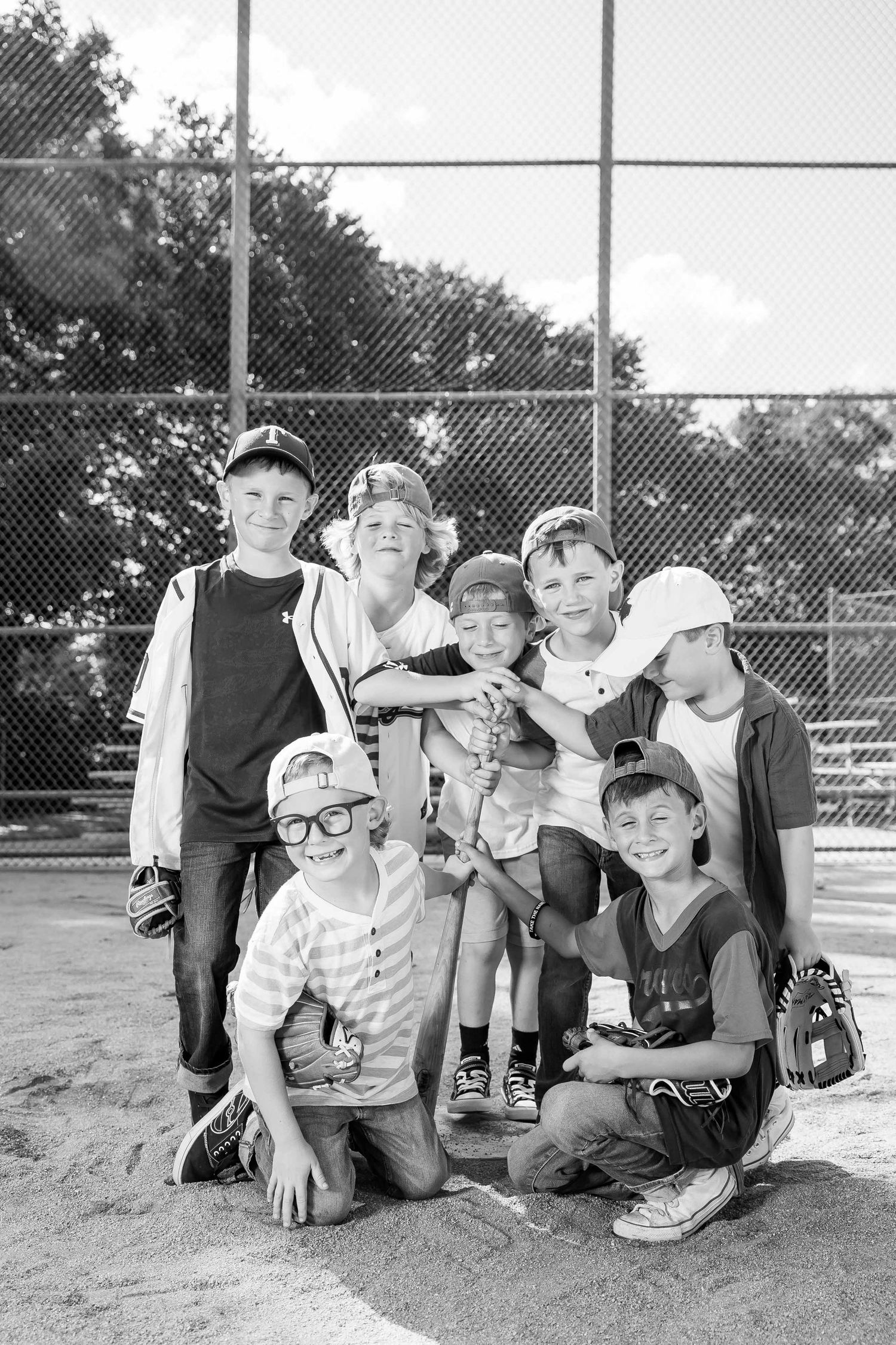 Black and white photo of a group of young boys in baseball gear posing together on a sandy baseball field.