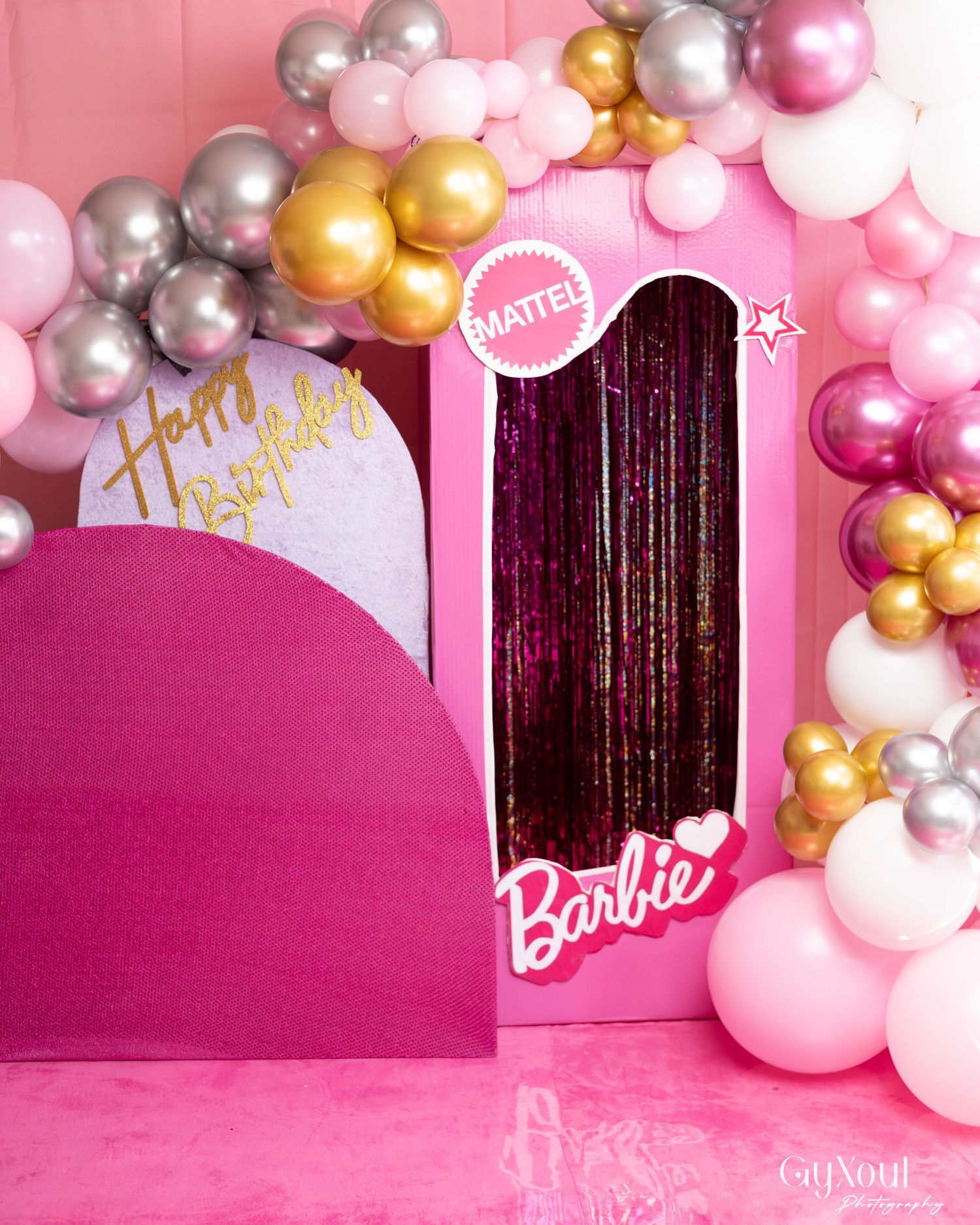 Barbie-themed birthday party setup with pink Mattel box, balloon garland in pink, gold, and silver, and Happy Birthday sign.