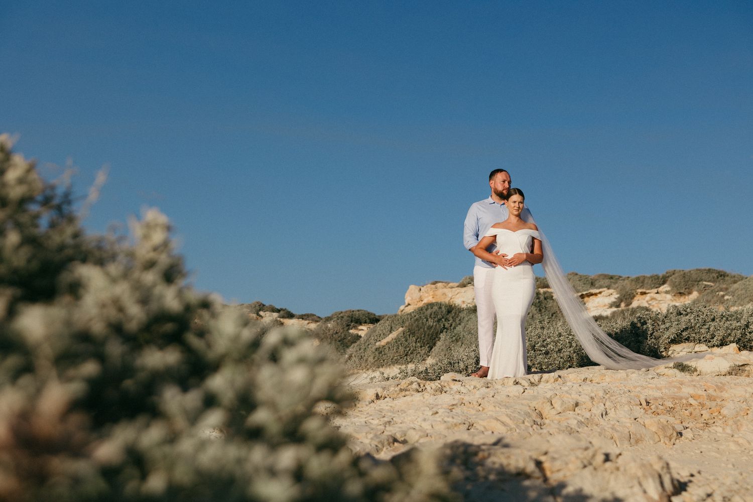 A couple stands atop a scenic desert cliff during a romantic photoshoot at sunset captured by a professional Cyprus wedding photographer.