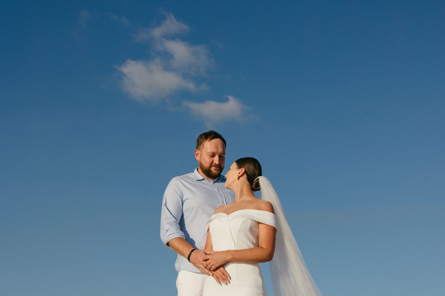 A romantic beachside photo session showing a couple in white attire embracing against a blue sky background in Paphos.