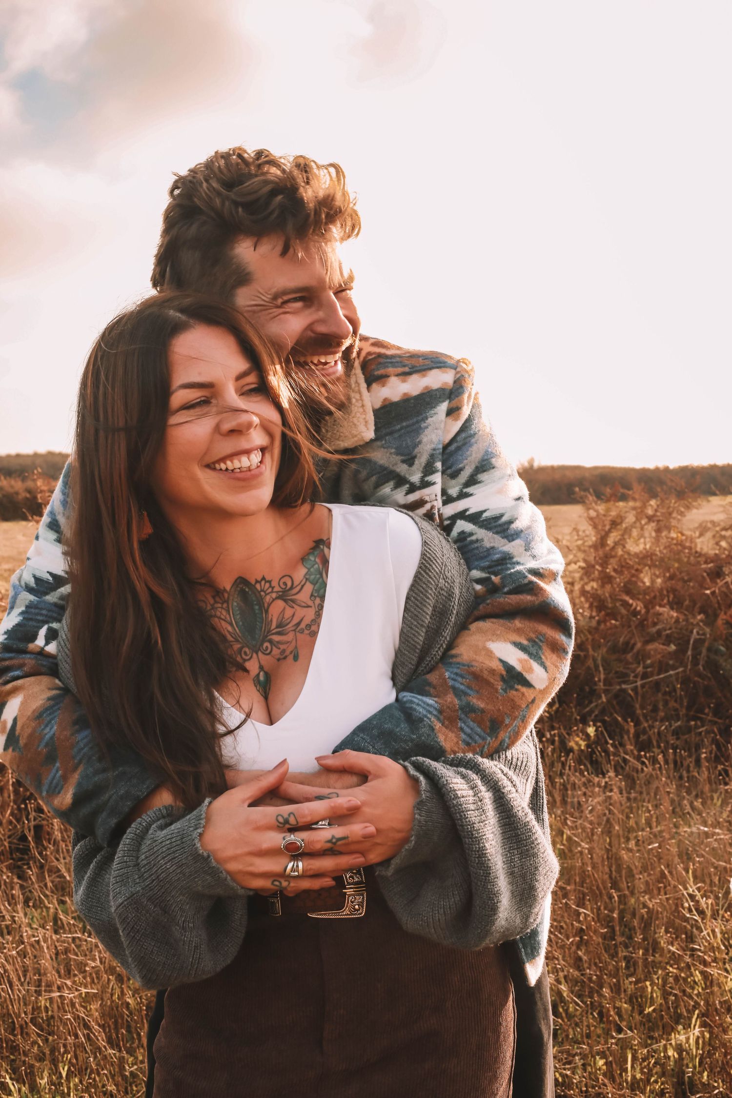 Couple embraces and laughs together in golden field during sunset photoshoot.