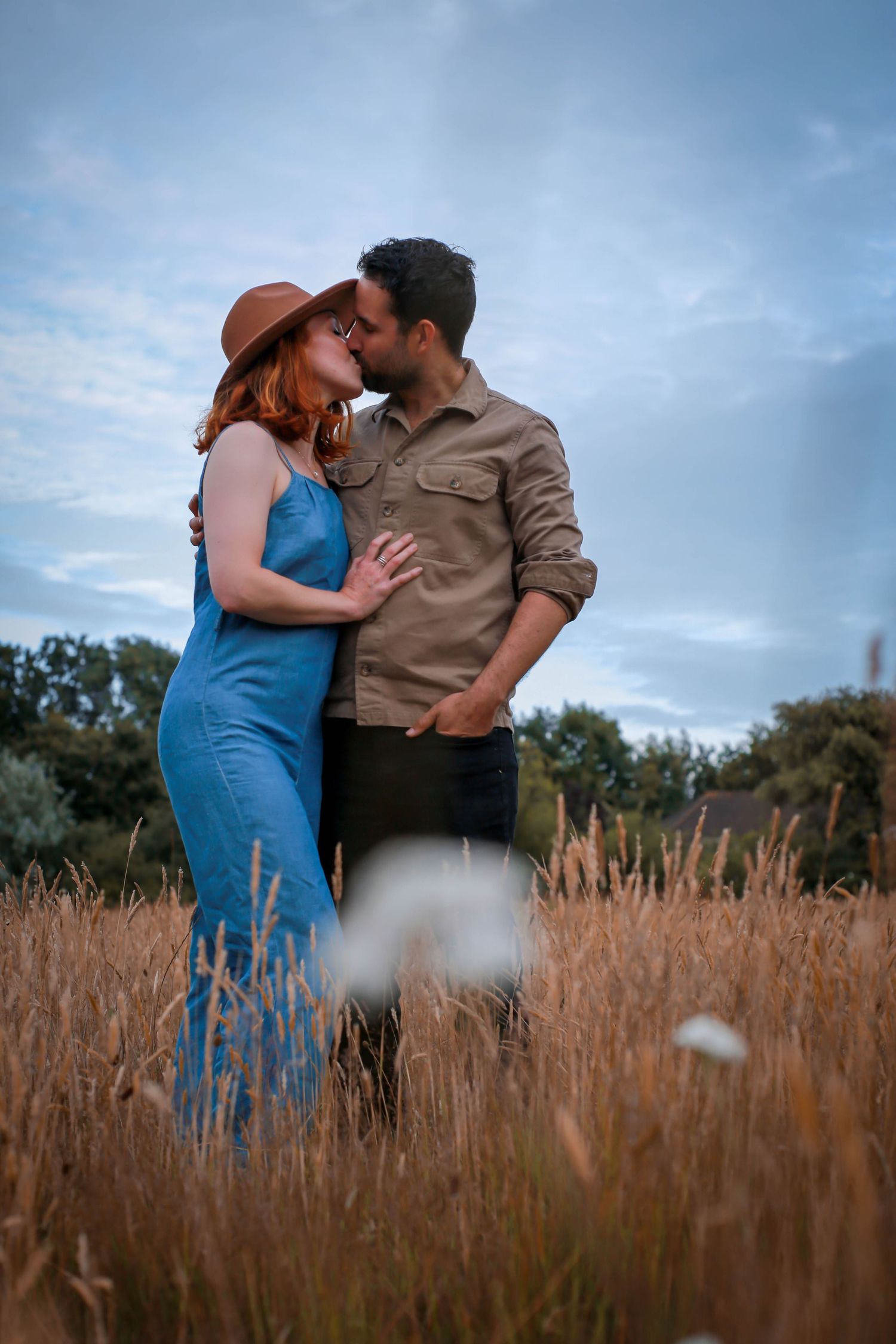 A couple shares an intimate moment together in a golden wheat field at sunset.
