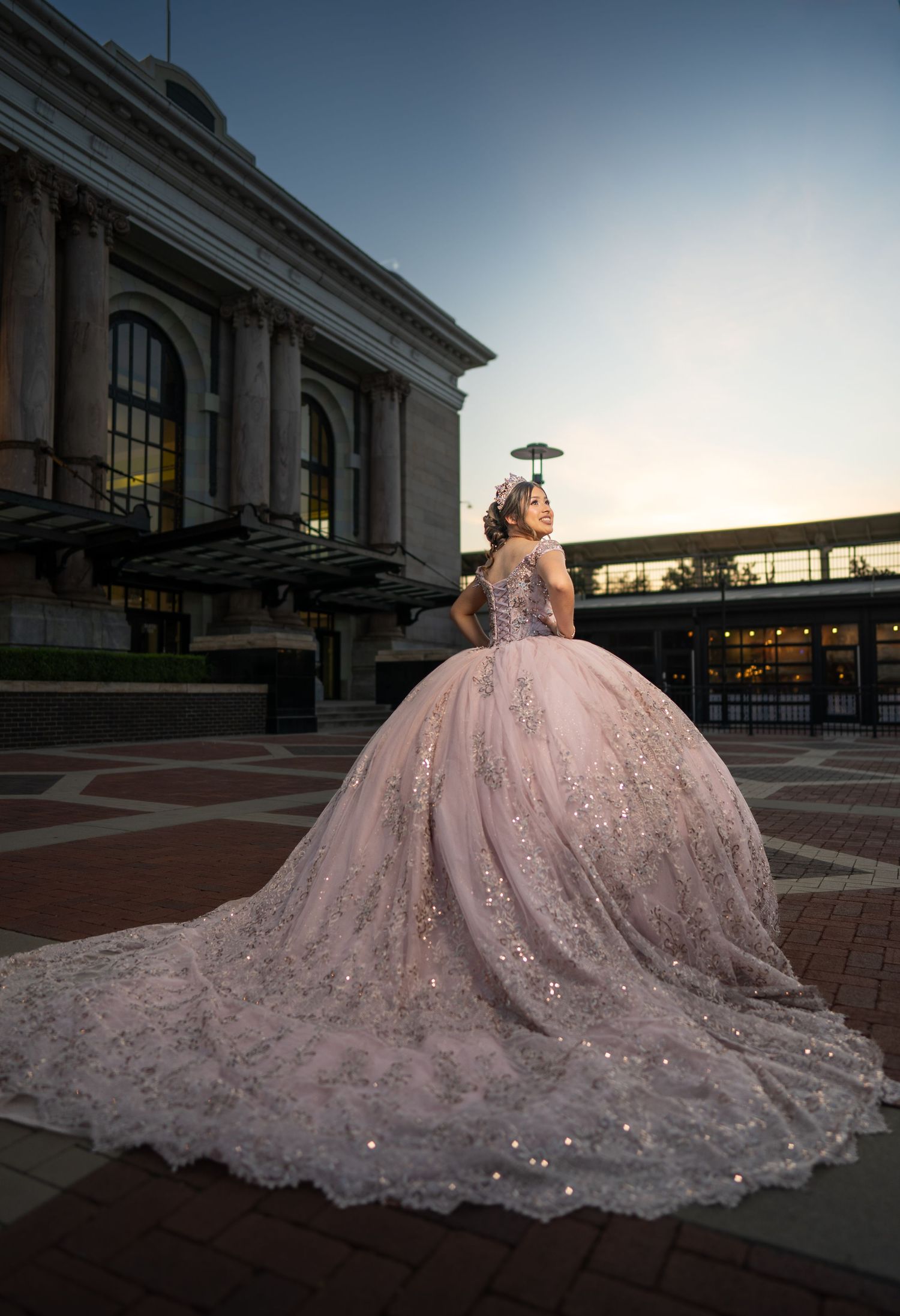 Dramatic pink ball gown with sparkly train photographed at sunset by classical building.