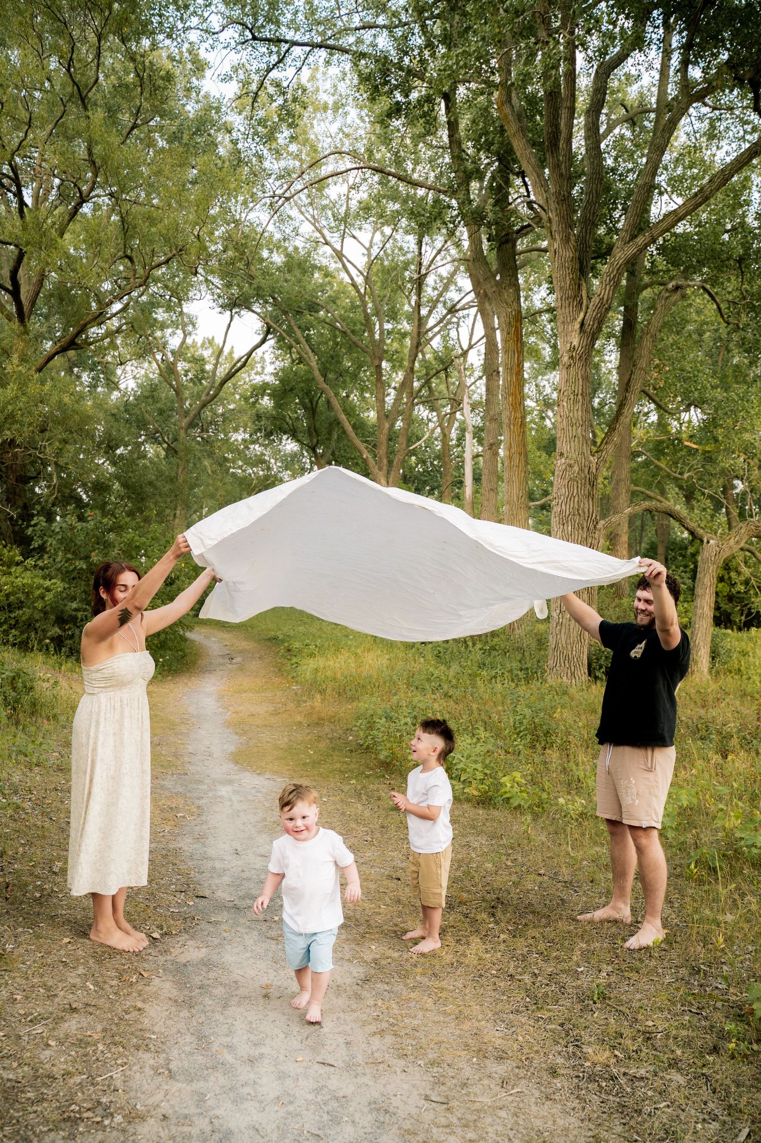 Family playing with white fabric in a wooded path creating artistic motion and movement in nature.