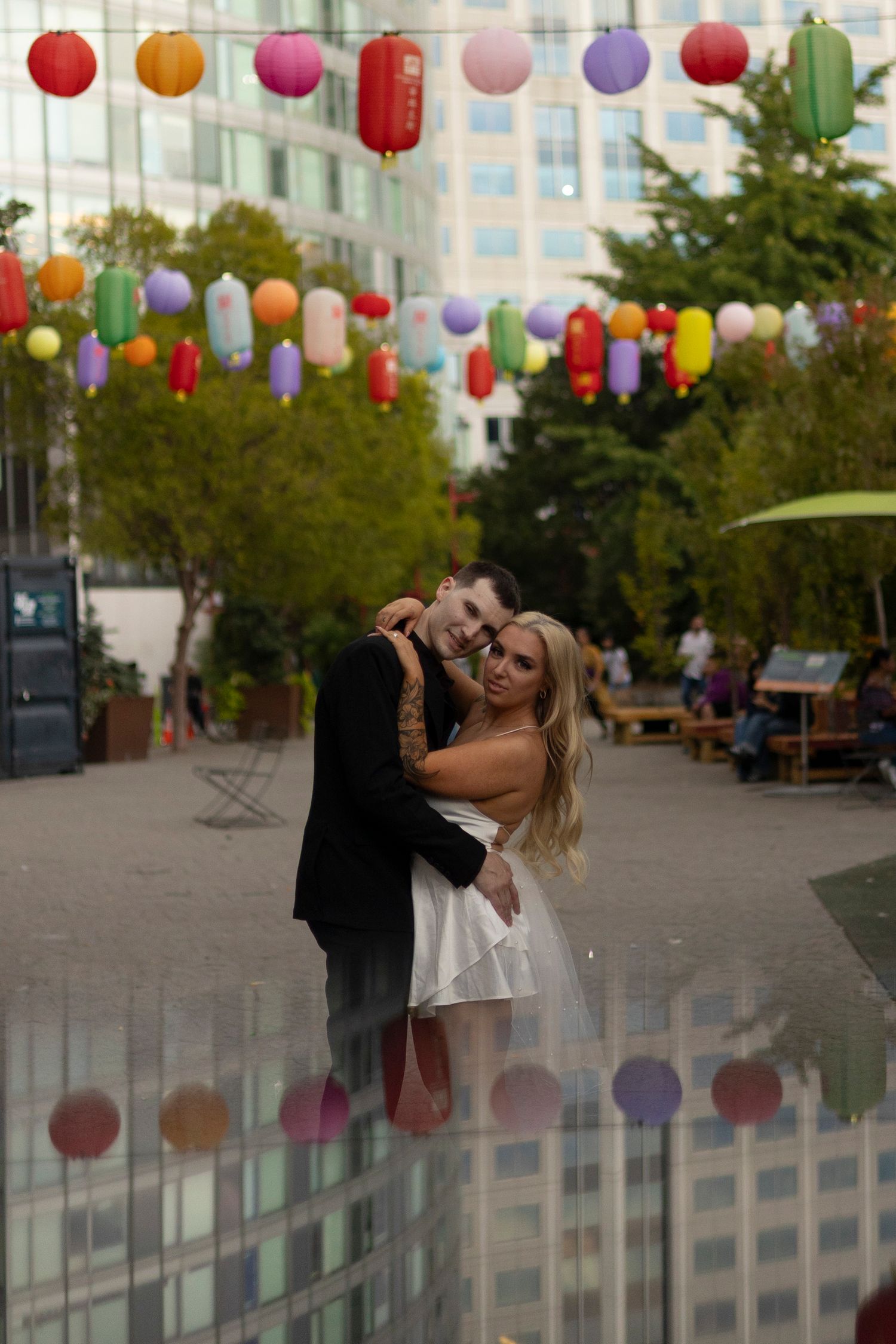 Colorful paper lanterns hang above a couple dancing and posing playfully in an urban setting.