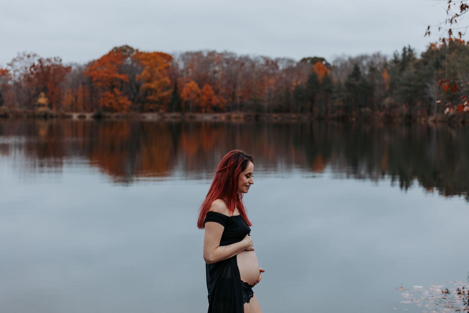 Autumn trees reflect in a still lake during a moody fall photoshoot.