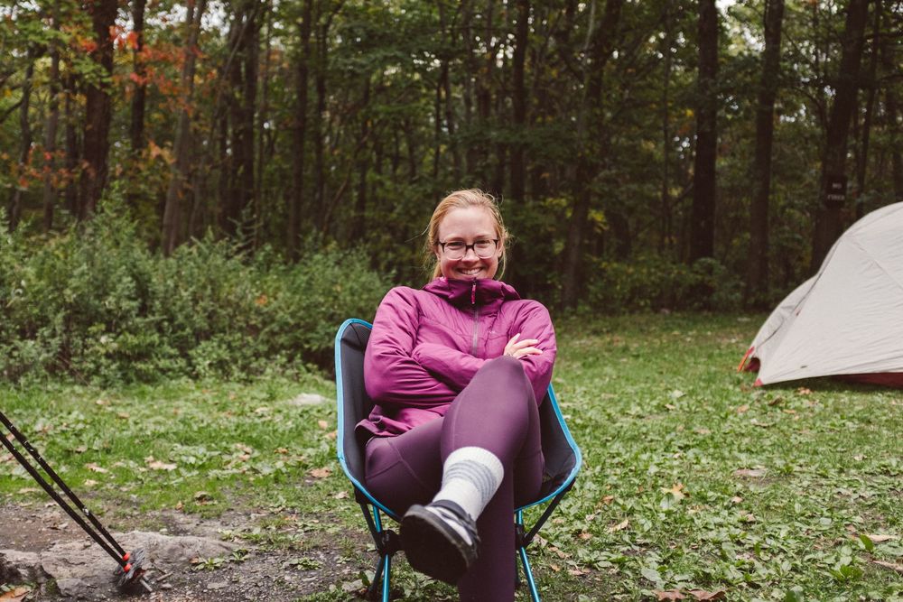 A person sits in a camping chair enjoying a relaxing moment in a wooded forest setting during autumn.